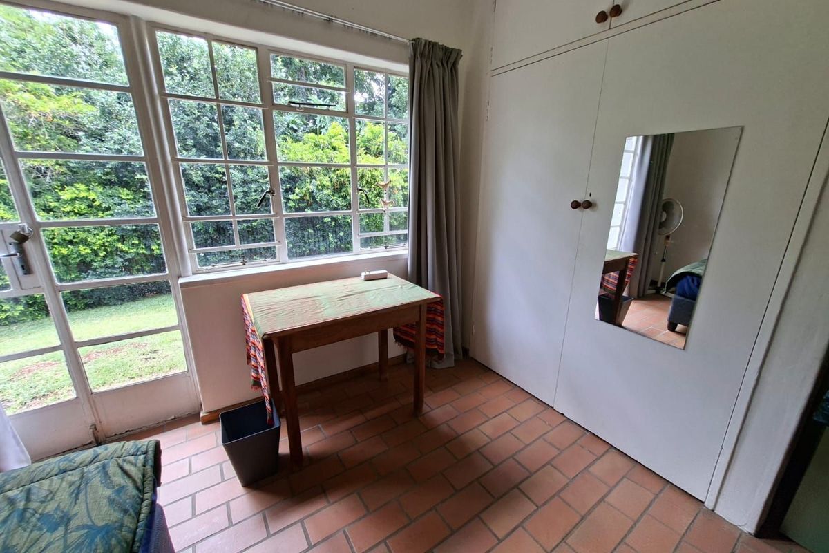 Bedroom featuring terracotta tiled flooring, built-in cupboards with integrated mirror, and large windows providing natural light and garden views.