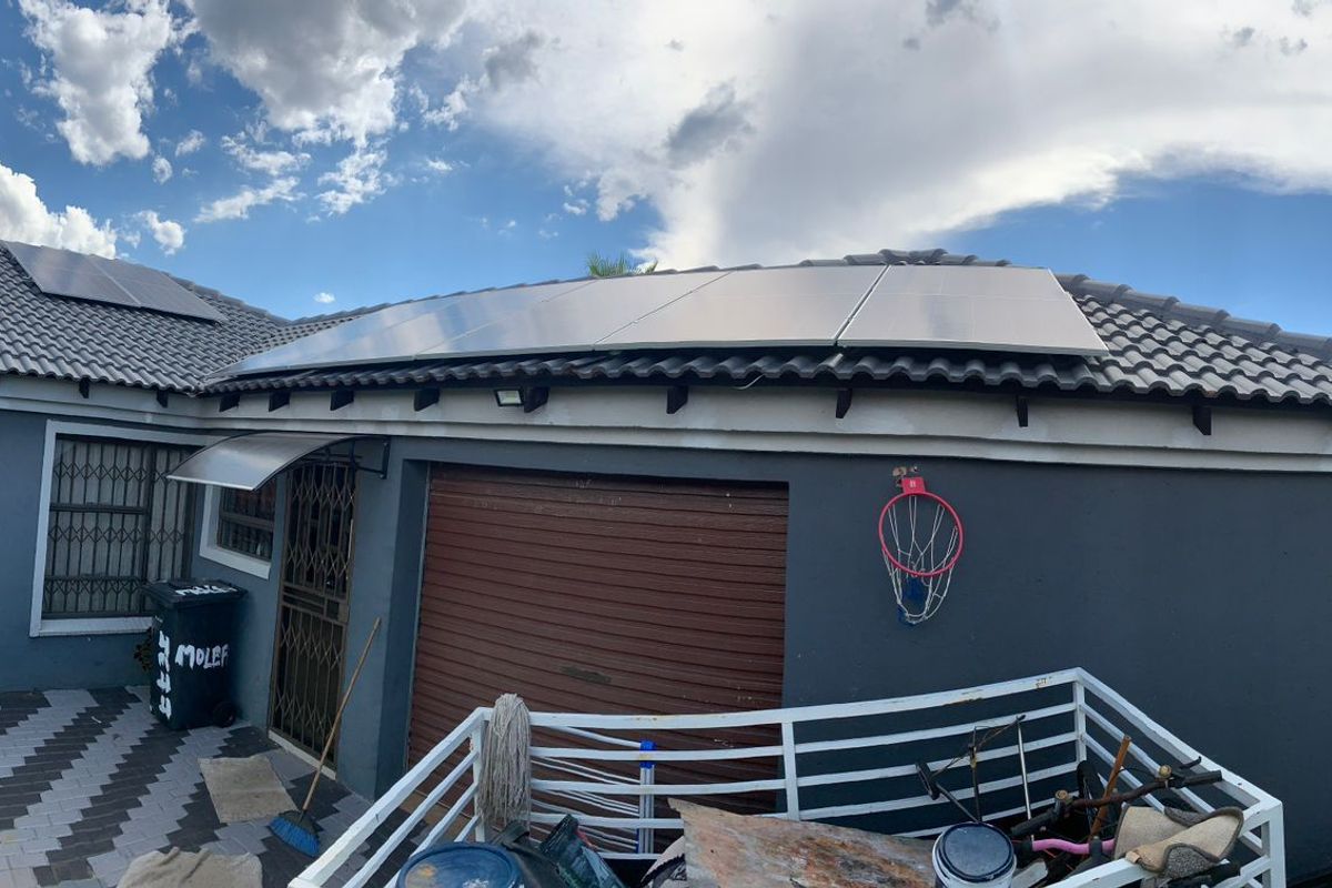 Rear exterior view of the house featuring a tiled roof with integrated solar panels, a roll-up garage door, and paved patio area.