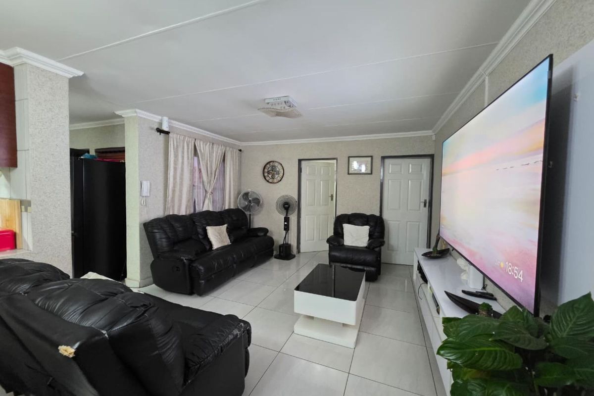 A spacious living room featuring tiled flooring, crown molding, and multiple access doors, providing a functional and well-lit central living area.