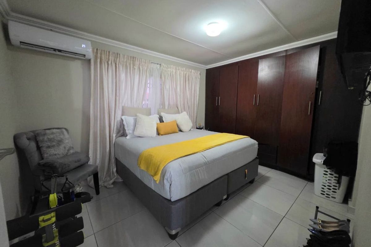 A well-maintained bedroom featuring large built-in wooden wardrobes, tiled flooring, and a wall-mounted air conditioning unit.