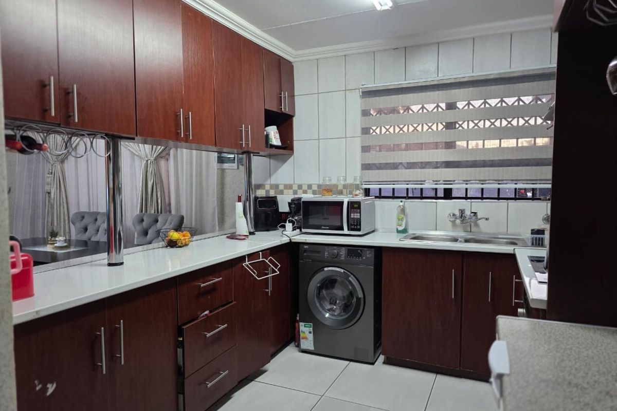 A functional kitchen featuring dark wood cabinetry, white countertops, a double basin sink, and an integrated washing machine.