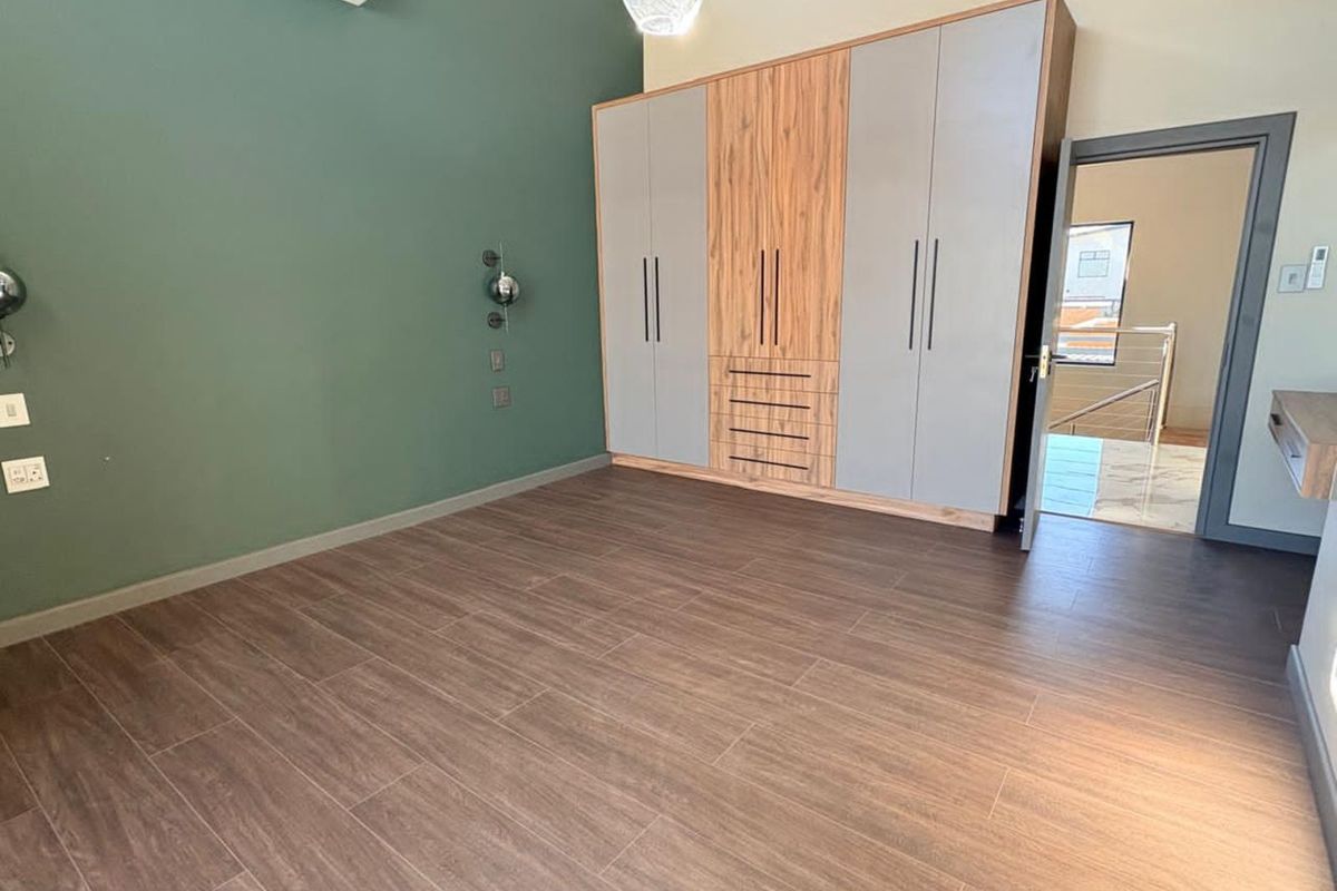 A modern bedroom featuring wood-look tile flooring, built-in floor-to-ceiling cabinetry with a mix of wood and grey finishes, and a wall-mounted air conditioning unit.