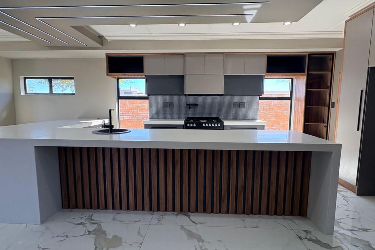 Modern kitchen featuring a large central island with stone countertop, integrated cabinetry, built-in gas hob, and stylish recessed ceiling lighting.