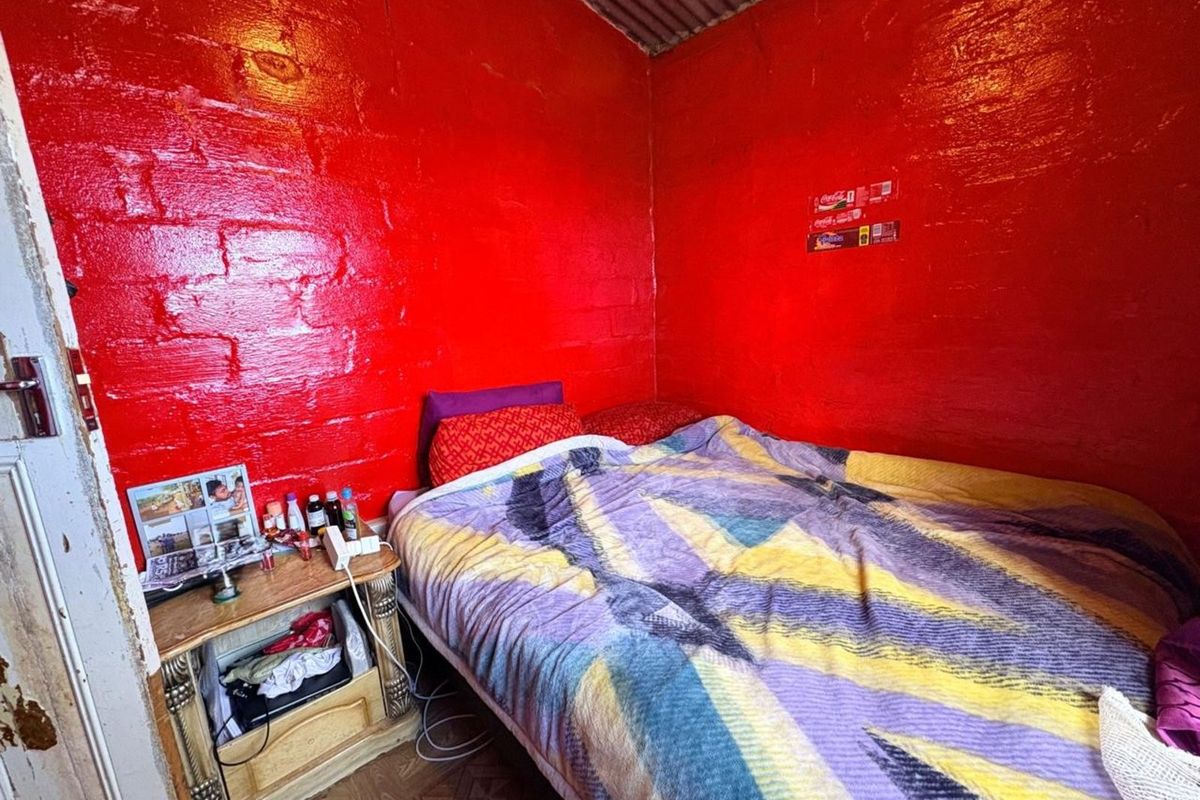 A compact bedroom featuring exposed painted brick walls, a corrugated metal ceiling, and tiled flooring.