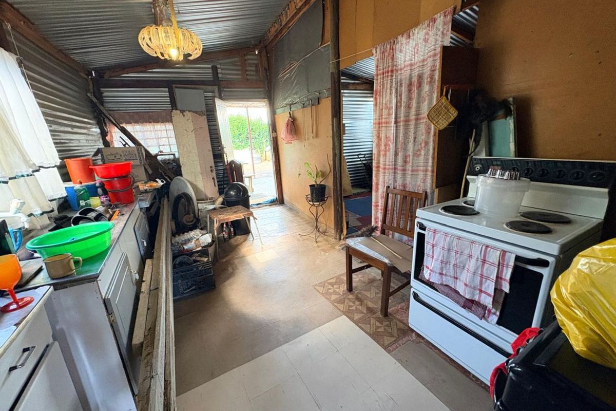 A rustic kitchen area featuring corrugated metal walls, basic cabinetry, and a freestanding electric stove, offering a functional but dated utility space.