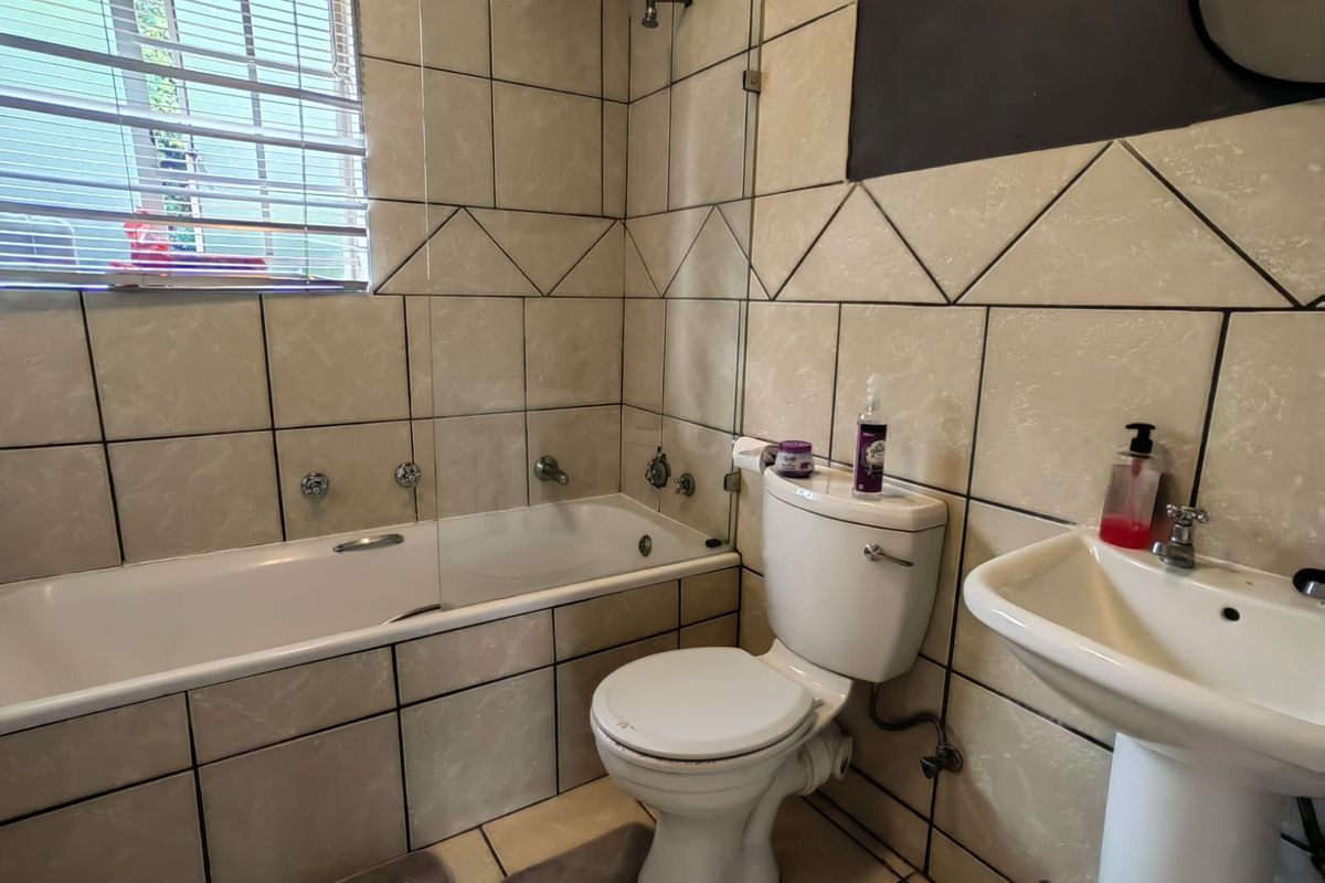 A functional bathroom featuring a bathtub with a glass shower screen, a pedestal basin, and a standard toilet, finished with neutral wall tiles.