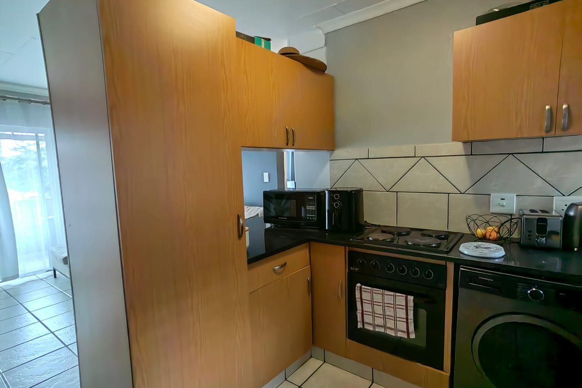 Compact kitchen featuring wood-look cabinetry, black countertops, built-in oven, hob, and integrated laundry appliance space.