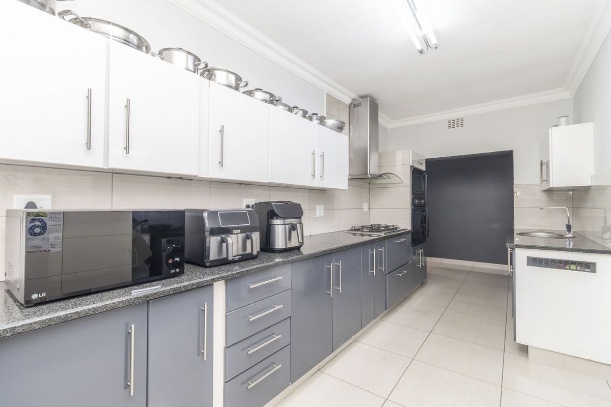 Modern kitchen featuring two-tone cabinetry, granite countertops, built-in oven, gas hob, and stainless steel extractor fan with tiled flooring.