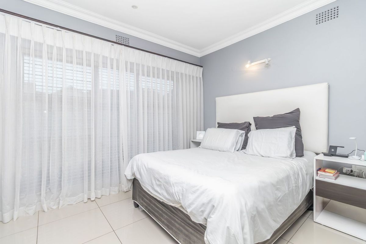 A bright and well-maintained bedroom featuring large sliding glass doors with sheer curtains, tiled flooring, and crown molding.