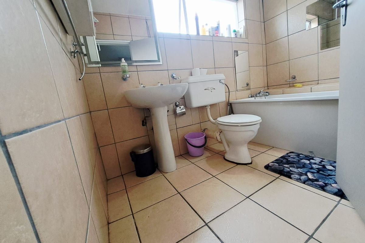 A dated bathroom featuring a pedestal basin, standard toilet, and bathtub with full-height wall tiling and tiled flooring.