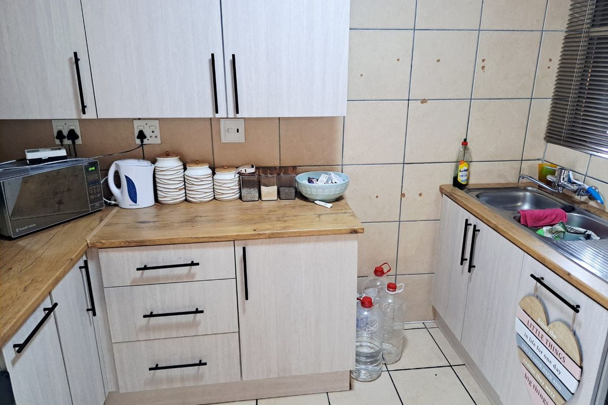 A functional kitchen area featuring light wood-grain cabinetry, wooden countertops, a double stainless steel sink, and tiled wall splashbacks.