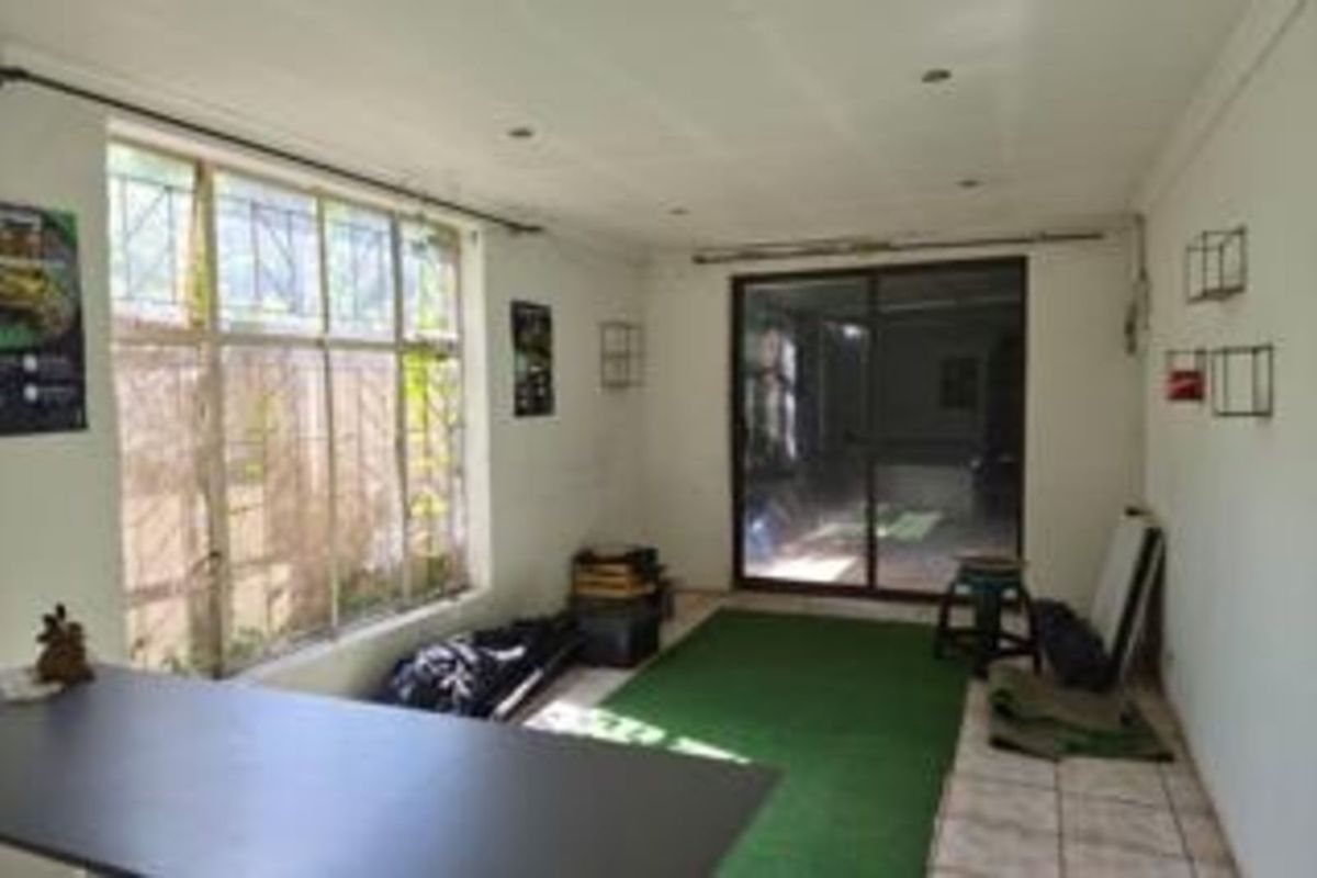 A spacious, sunlit living area featuring large windows, sliding glass doors, and tiled flooring, offering potential for a modern renovation.