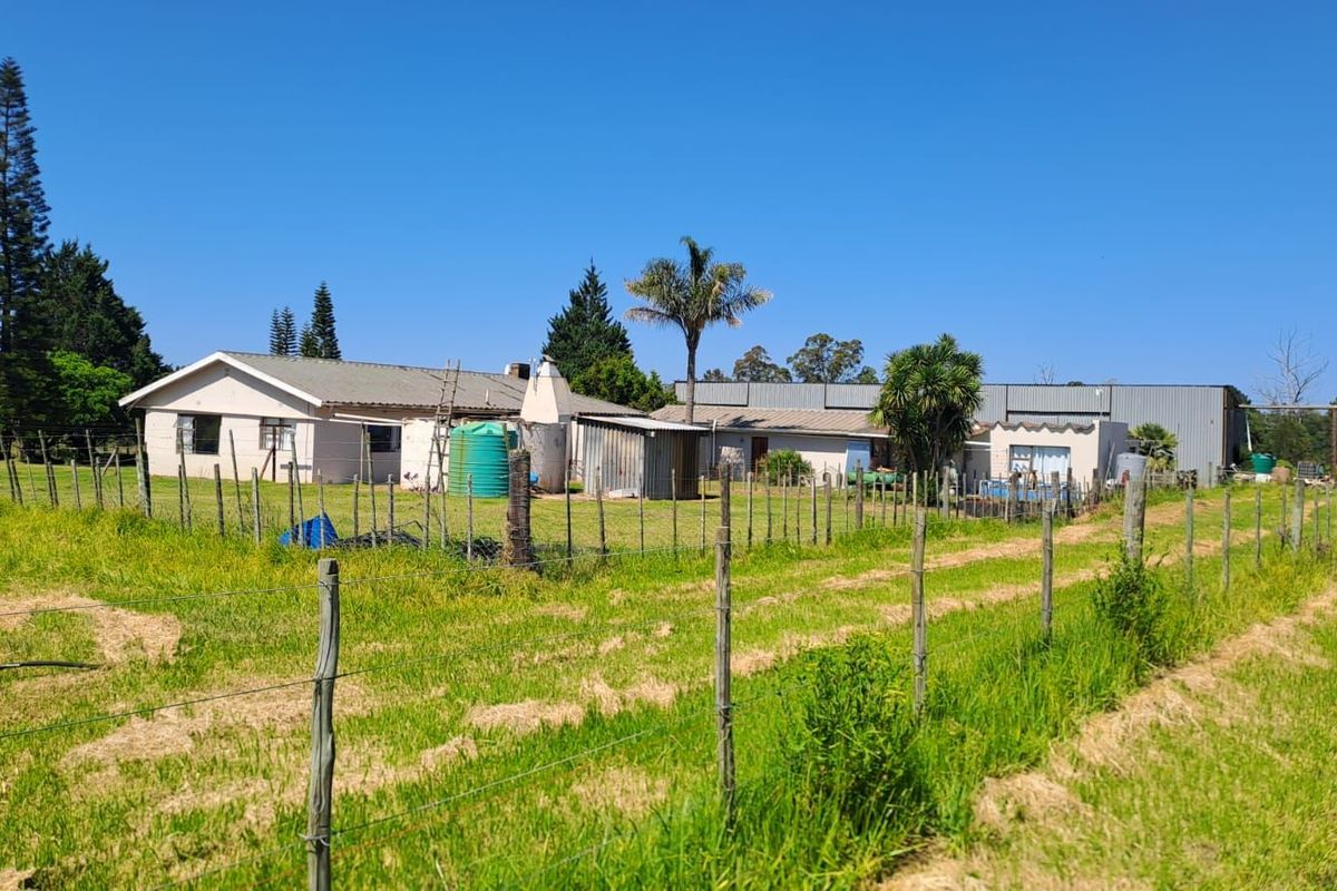 A wide view of a farm property featuring a main residence, adjacent outbuildings, and a large water storage tank set within a fenced rural landscape.