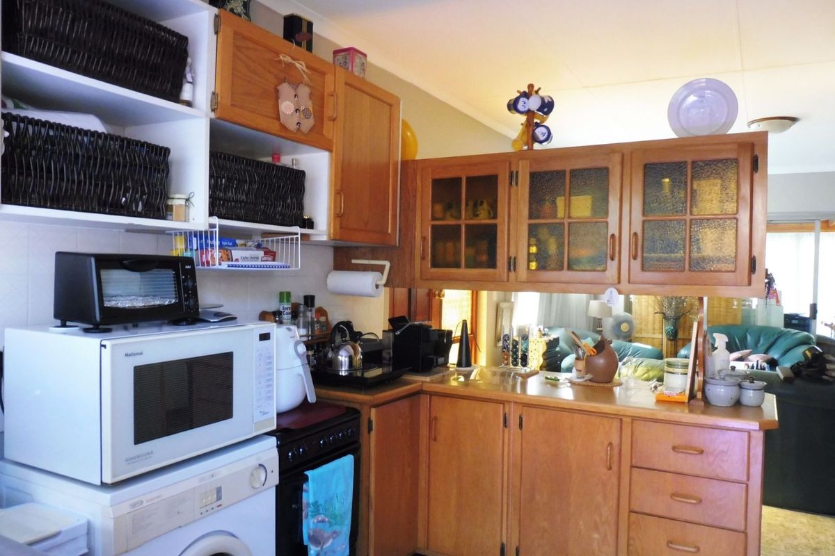 A functional kitchen featuring wooden cabinetry, integrated storage, and a compact layout with a pass-through window overlooking the adjacent living area.