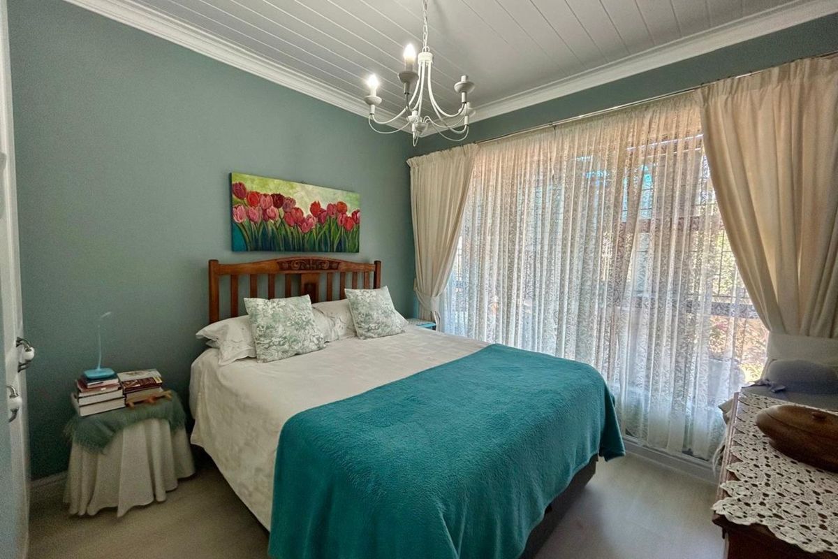 A well-maintained bedroom featuring a classic chandelier, tongue-and-groove ceiling, and large window with sheer curtains, providing a bright and comfortable living space.