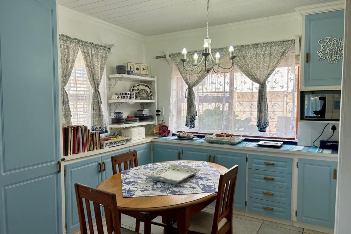 A cozy kitchen featuring light blue cabinetry, tiled flooring, built-in shelving, and a dedicated dining area with a chandelier.