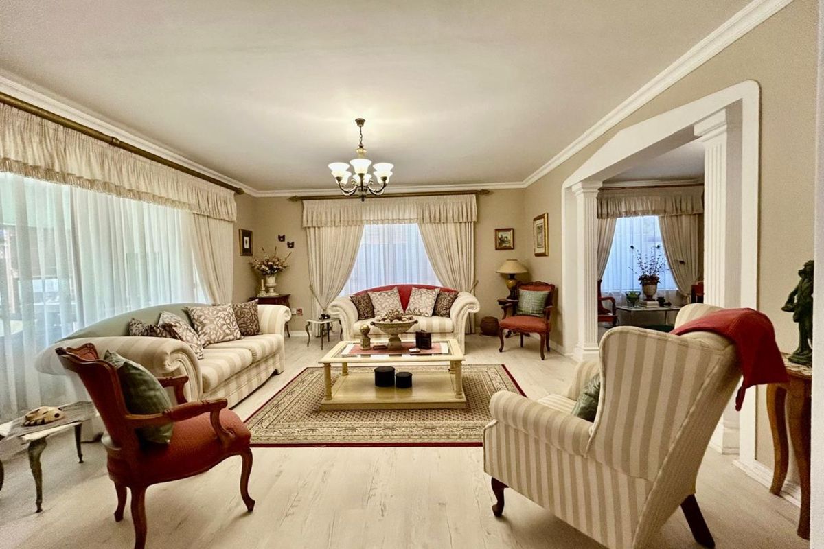 Spacious living room featuring light-toned wood-look flooring, decorative crown molding, and an open-plan layout connecting to an adjacent room through a columned archway.