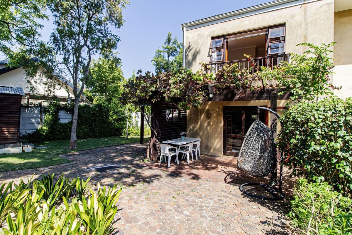 Rear view of the property featuring a paved patio area, a timber pergola with climbing vines, and a balcony overlooking the garden.