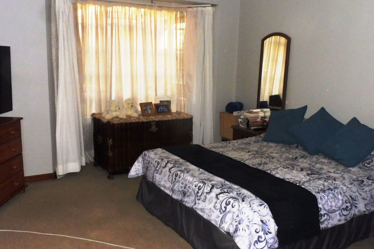 A spacious bedroom featuring neutral wall tones, a large bay window with natural light, and fitted carpet flooring.