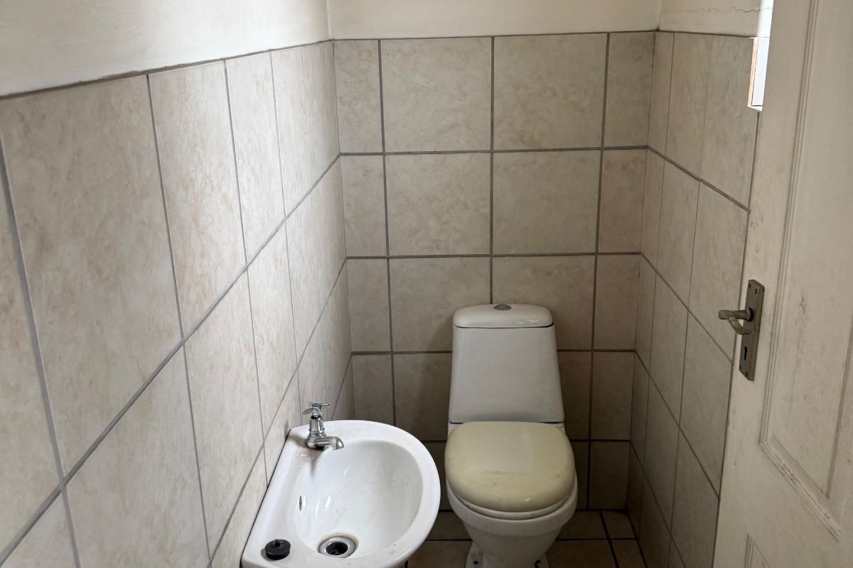 A compact industrial restroom featuring a wall-mounted basin and a standard toilet with tiled walls and flooring.