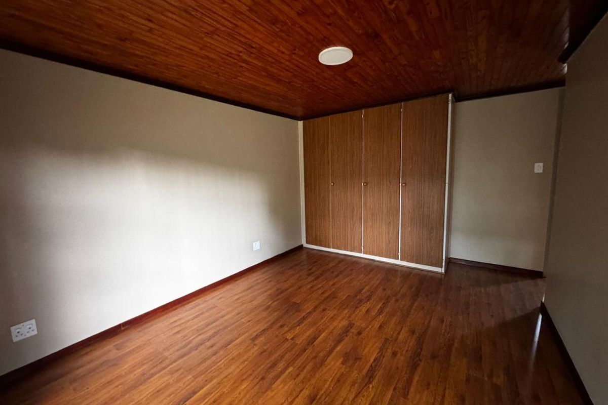 A spacious bedroom featuring warm timber laminate flooring, a wood-paneled ceiling, and built-in wooden wardrobes.