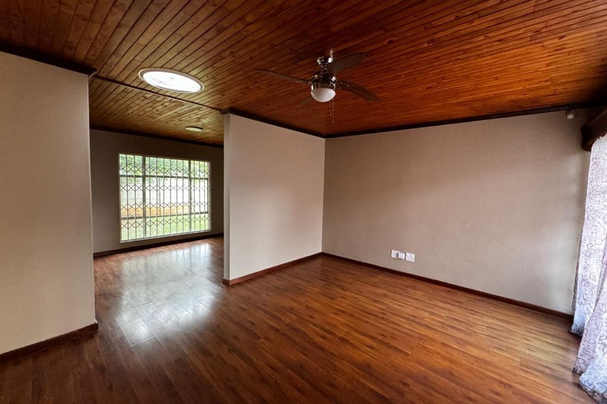 Spacious living area featuring warm wood-paneled ceilings, laminate flooring, and a ceiling fan, offering a versatile layout with natural light.