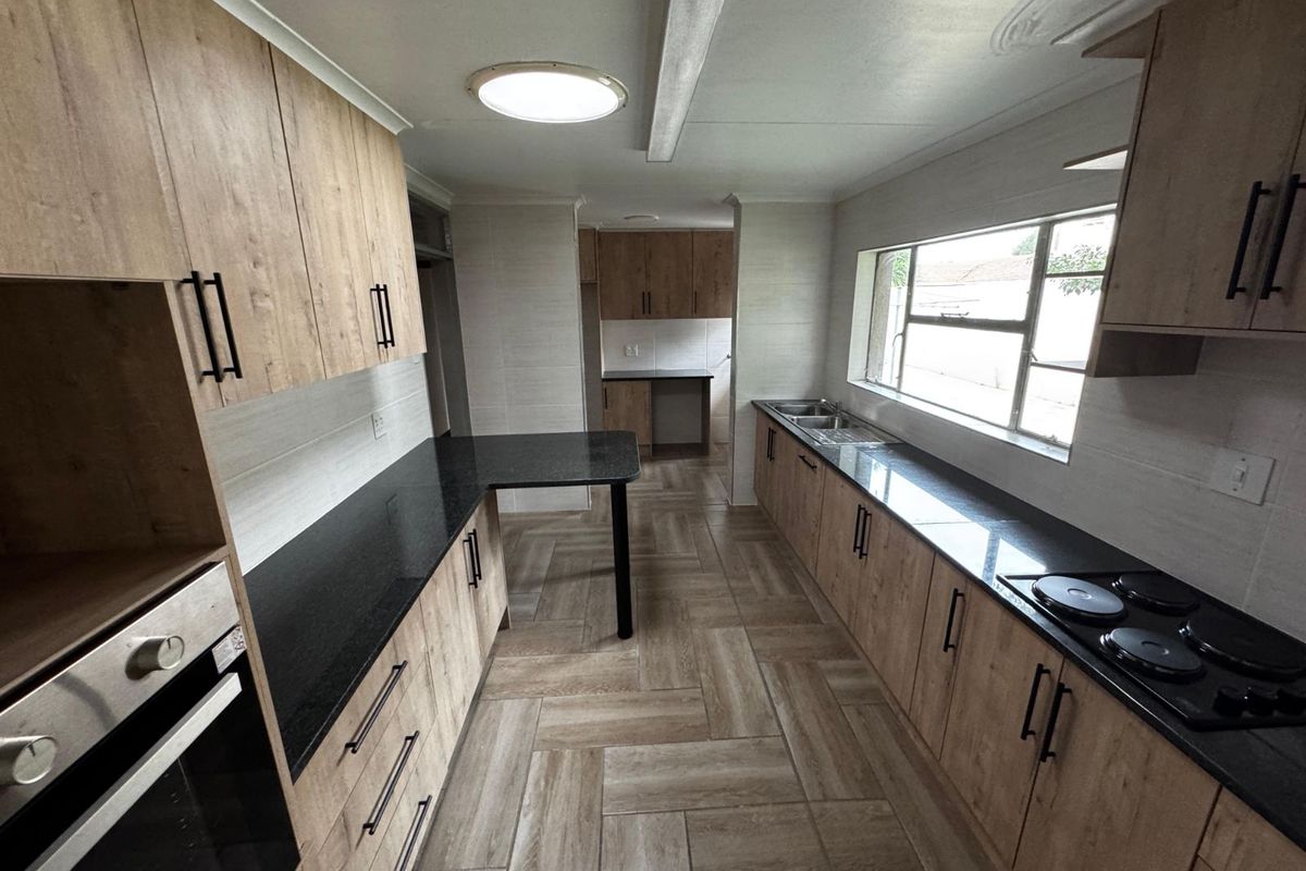 Modern kitchen featuring wood-look cabinetry, dark granite countertops, a built-in oven, and a black electric hob with a double sink.