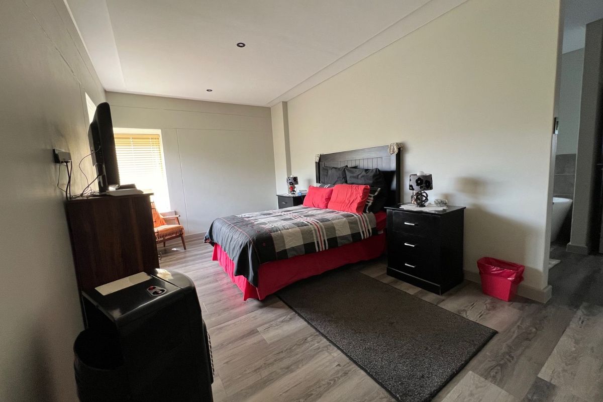 A spacious bedroom featuring wood-look laminate flooring, recessed ceiling lighting, and an en-suite bathroom area visible in the background.