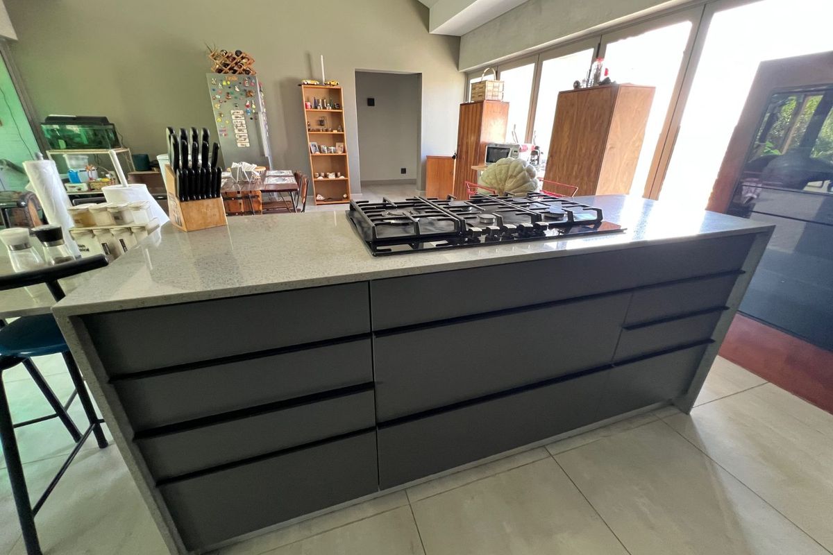 Modern kitchen featuring a large central island with a built-in gas hob, sleek dark cabinetry, and large format floor tiles.