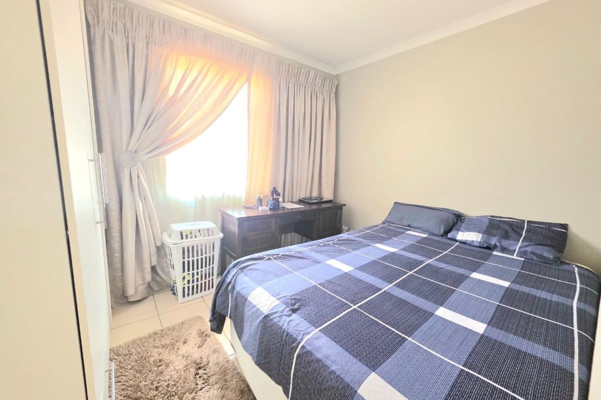 A functional bedroom featuring tiled flooring, built-in cupboard space, and a window with curtain treatments.