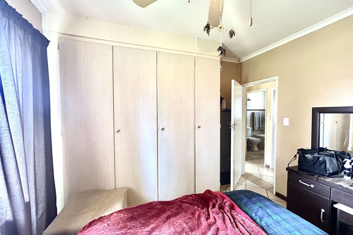 A bedroom featuring built-in wooden wardrobes, a ceiling fan, and an adjoining bathroom with tiled flooring.