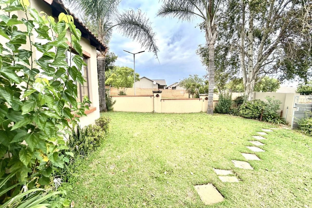 A private rear garden featuring a lawn, established trees, and a perimeter boundary wall, providing a quiet outdoor space for the townhouse.