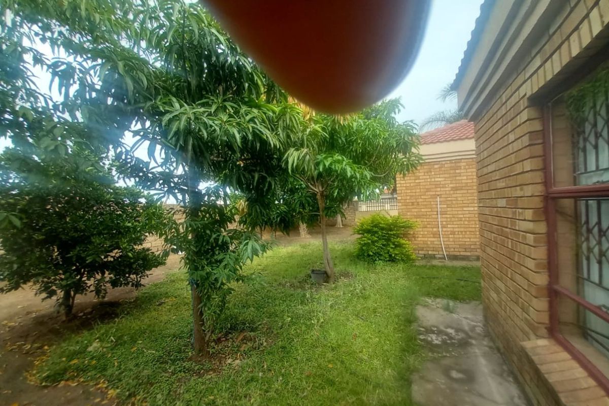A view of the rear garden area featuring established trees, lawn, and brick exterior walling of the house.