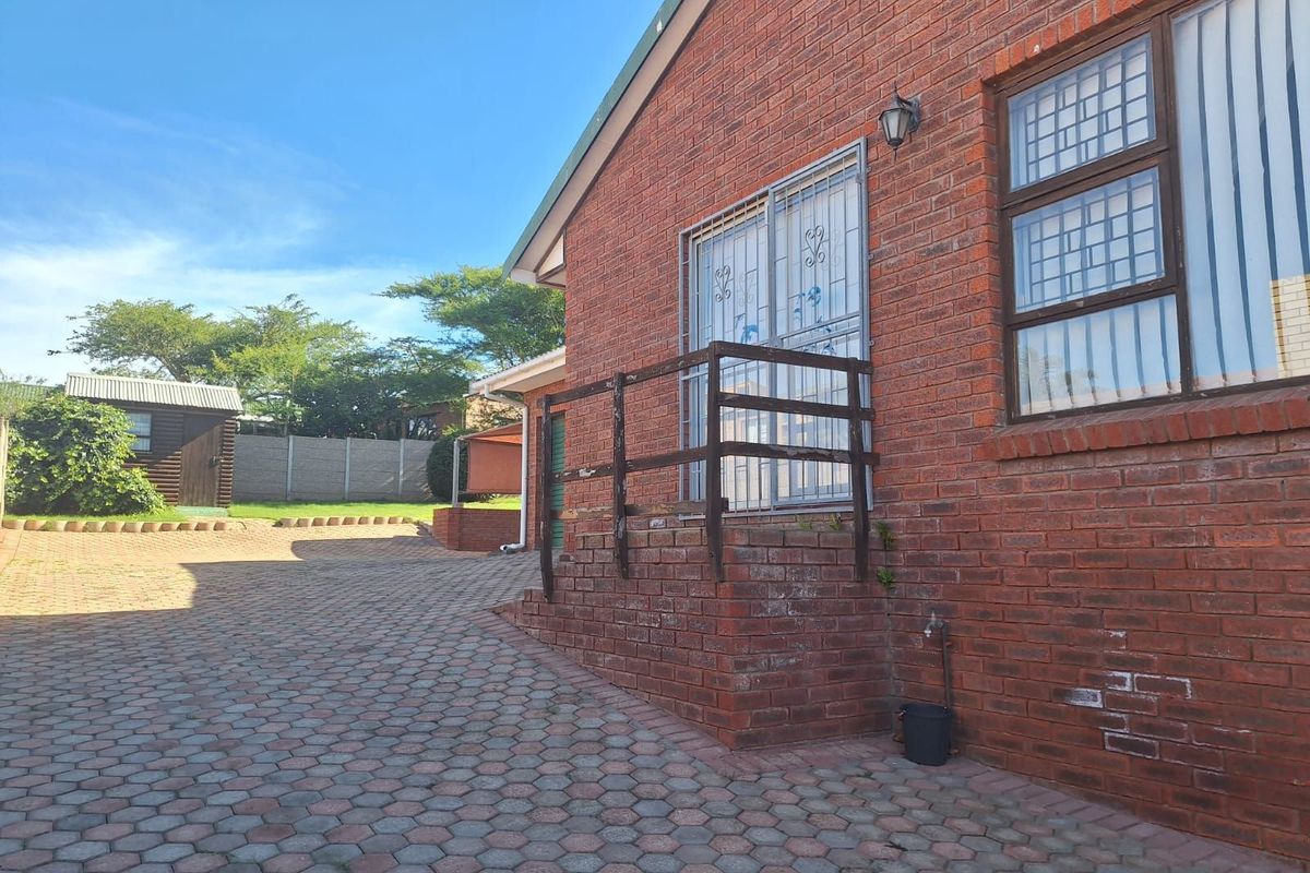 Rear exterior view of the property featuring a paved courtyard, brick facade, and a raised entrance with a timber railing.