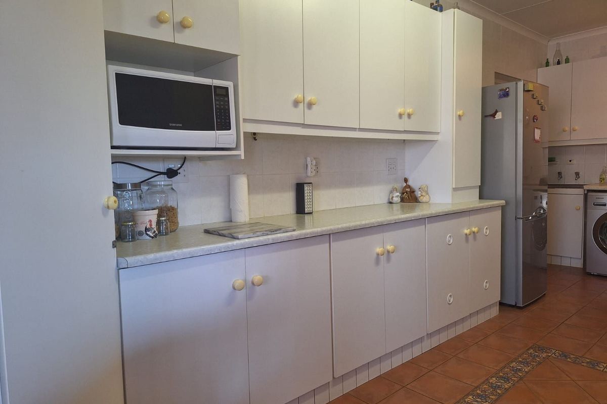 A functional kitchen featuring white cabinetry, laminate countertops, and tiled flooring, providing ample storage and workspace for daily meal preparation.