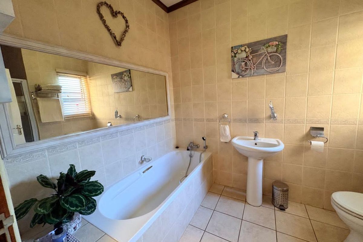 A functional bathroom featuring a built-in bathtub, pedestal basin, and toilet, finished with neutral wall and floor tiles.