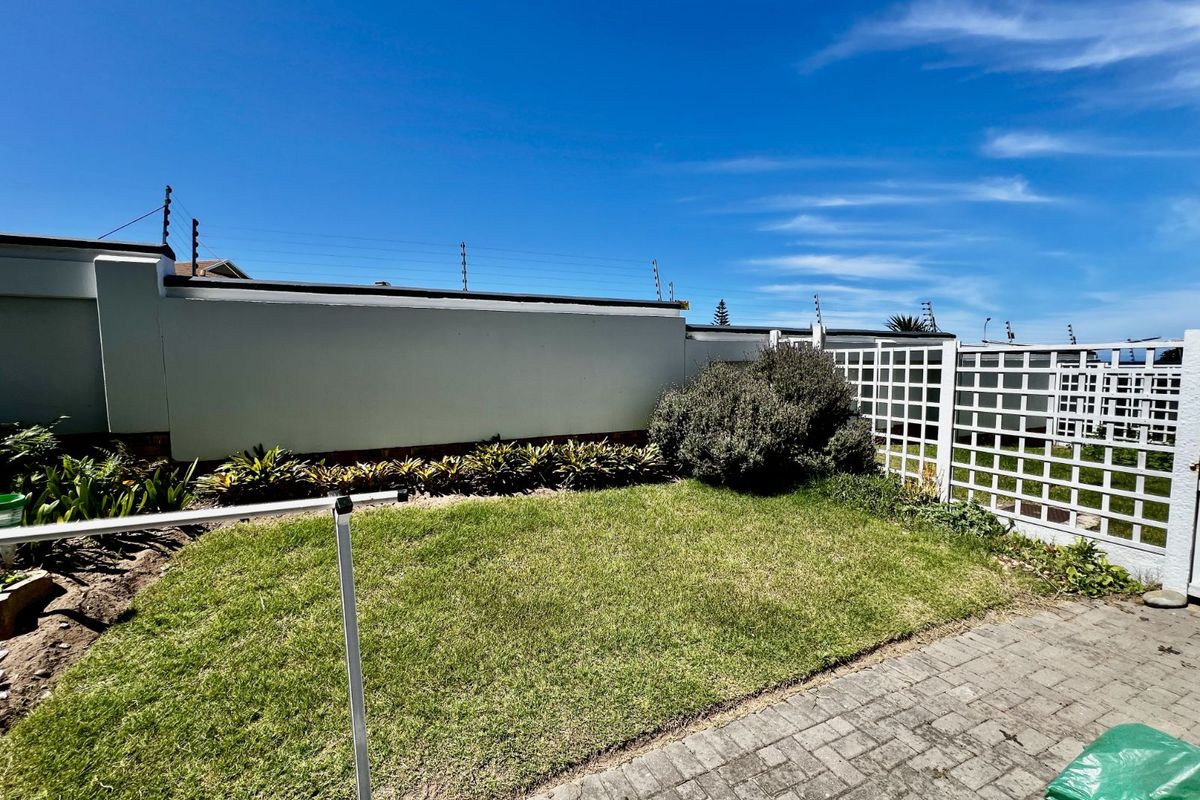 A private rear garden featuring a small lawn, paved patio area, and perimeter boundary walls with security fencing.