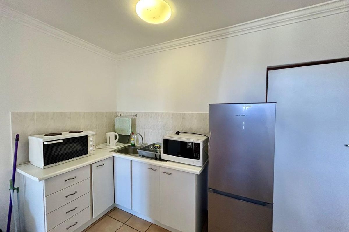 A compact kitchen area featuring white cabinetry, tiled splashback, stainless steel sink, and tiled flooring.