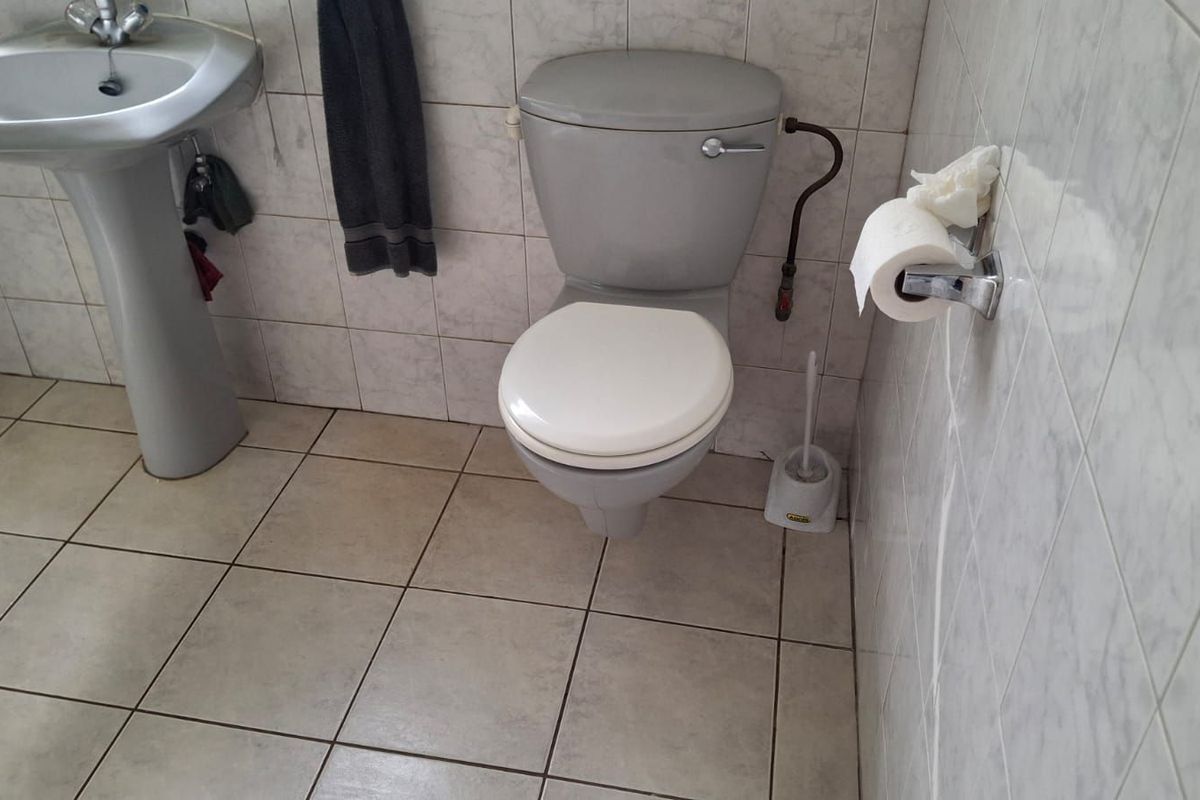 A functional bathroom featuring a pedestal basin and toilet with tiled walls and flooring, presenting an opportunity for modernization.