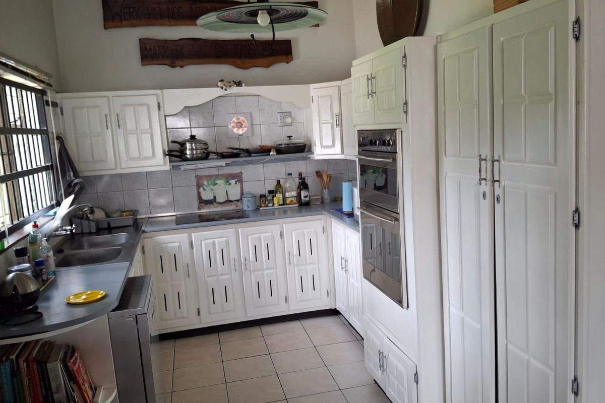 A functional kitchen featuring white cabinetry, built-in double oven, integrated hob, tiled splashbacks, and tiled flooring.