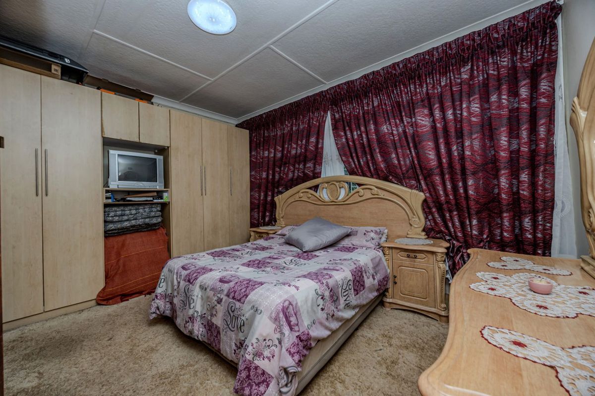 A bedroom featuring built-in wooden wardrobes, carpeted flooring, and a panelled ceiling.