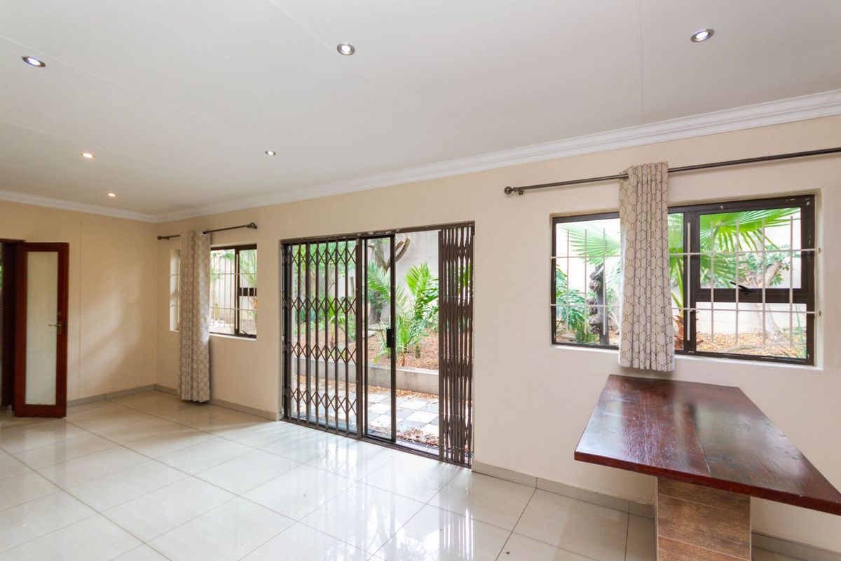 Spacious living area featuring tiled flooring, recessed ceiling lighting, and sliding glass doors with security gates opening to the rear garden.
