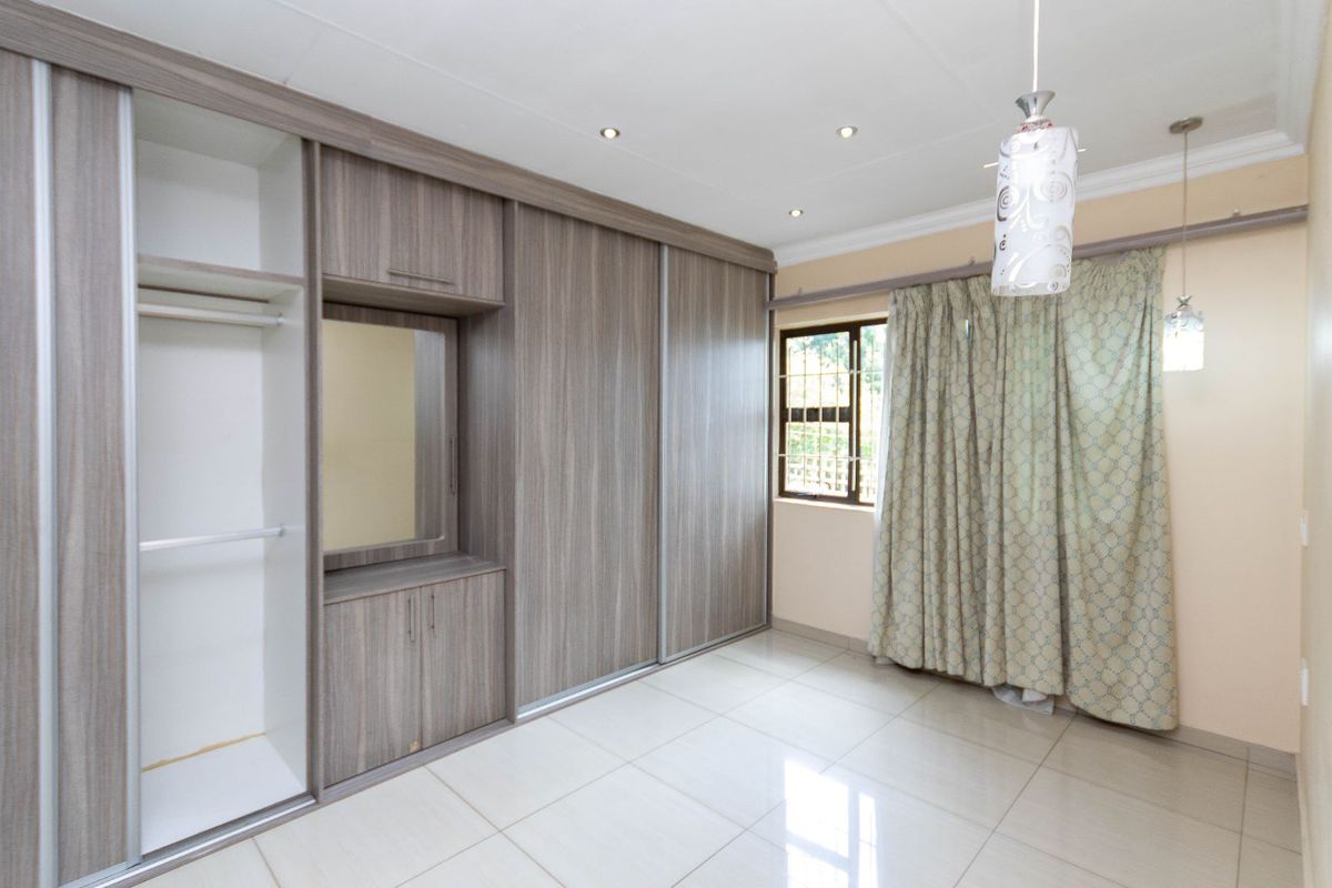 A bright bedroom featuring large built-in wooden wardrobes with sliding doors, tiled flooring, and recessed ceiling lighting.