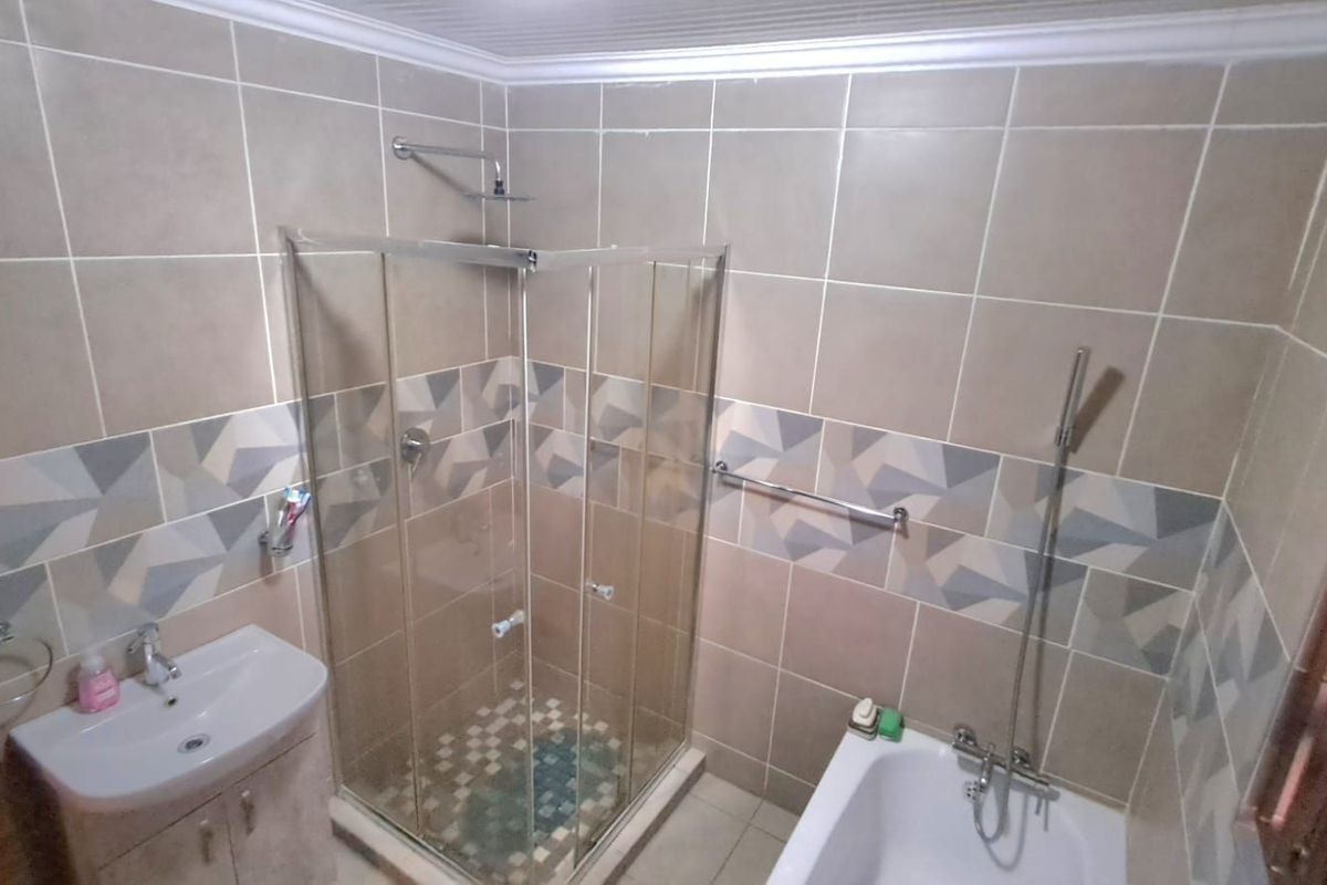 A functional bathroom featuring a glass-enclosed shower, a separate bathtub, and a vanity basin with tiled walls.