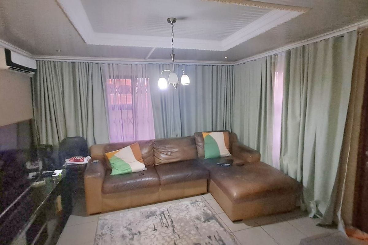 A living room featuring tiled flooring, a tray ceiling with recessed lighting, and a wall-mounted air conditioning unit.