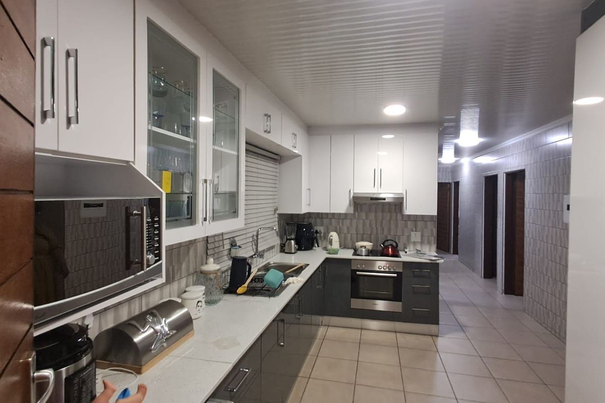 Modern kitchen featuring white and grey cabinetry, stone countertops, built-in oven, extractor fan, and tiled flooring, leading into a hallway.