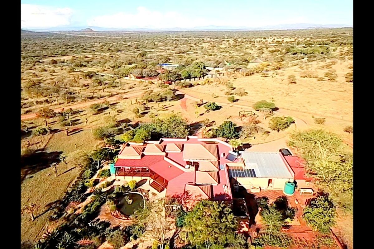 Aerial view of a farm property featuring a main residence with a red roof, solar panels, and surrounding landscaped grounds in a rural setting.