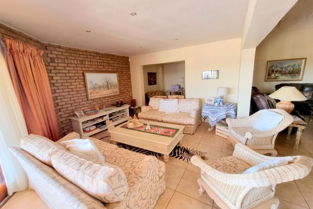 A spacious living room featuring a rustic exposed brick feature wall, tiled flooring, and recessed ceiling lighting, creating a warm and inviting atmosphere.