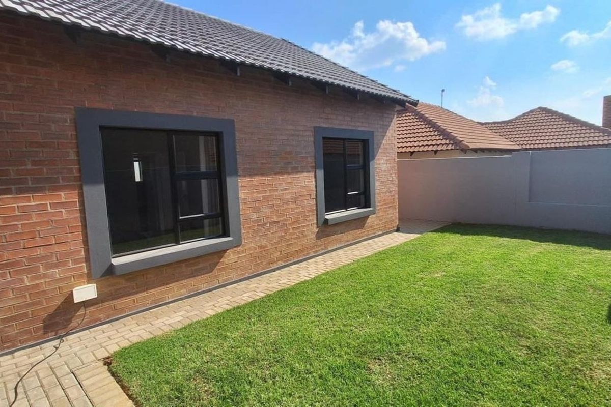 A well-maintained rear exterior view featuring exposed brickwork, modern dark-framed windows, a paved walkway, and a neat lawn area.