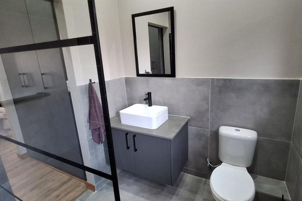 Modern bathroom featuring a floating vanity with a vessel sink, black fixtures, a walk-in shower with a black-framed glass screen, and grey tiling.